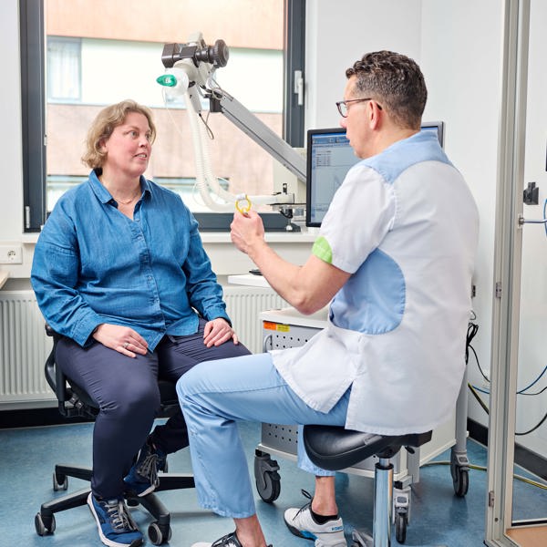 Patiënte zit op stoel, tegenover haar zit zorgverlener. Tussen hen in staat een medisch hulpmiddel. Ze kijken elkaar aan. THEMA vormt de 'linking pin' tussen de Anna Zorggroep en haar zorgpartners